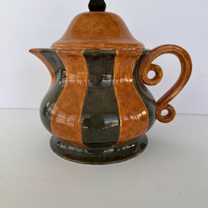 May include: A brown and black striped ceramic teapot with a black knob on the lid.