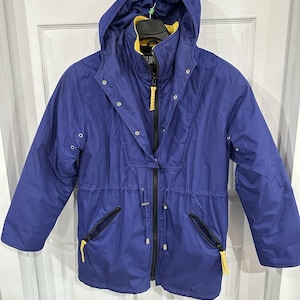 May include: A blue hooded jacket with a yellow interior lining and yellow zipper accents. The jacket has a drawstring waist, two zippered pockets, and snap closures. The jacket is hanging on a hanger.