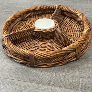 May include: A round, woven wicker serving tray with four divided sections and a central white ceramic bowl. The tray is a warm brown colour and appears to be handmade. The tray is approximately 35 cm in diameter.