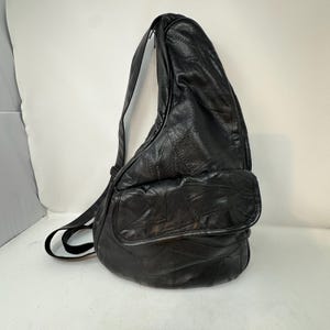 May include: A black leather sling backpack featuring a teardrop shape, a single adjustable shoulder strap, and a front flap pocket. The exterior is constructed from multiple stitched leather panels, creating a textured, patchwork-style surface.