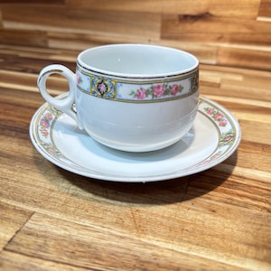 May include: A white ceramic mug with a black handle and the text "But first, coffee" in a handwritten style. The mug is on a white surface. The mug is likely for hot beverages.