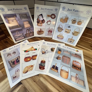 May include: Several issues of "Just Patterns" magazine, showcasing basket-making designs. The covers display images of woven baskets, decorative items, and seasonal themes. The magazines are arranged on a wooden surface.