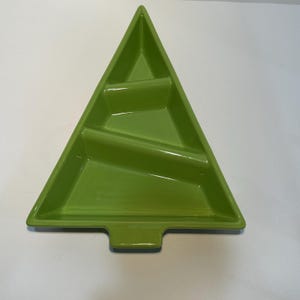Pode incluir: Um prato de servir verde brilhante, triangular, em forma de árvore de Natal. O prato tem três compartimentos separados e uma pequena base retangular. O acabamento brilhante reflete a luz.