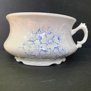 Pode incluir: Pote de cerâmica branco com um design floral azul e uma alça.