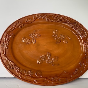 May include: A large, oval, brown ceramic serving platter with a raised, embossed design of vines and berries around the edge.