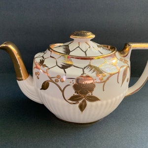 Peut inclure: Théière blanche avec des motifs floraux et géométriques dorés. La théière a une poignée et un bec verseur dorés.