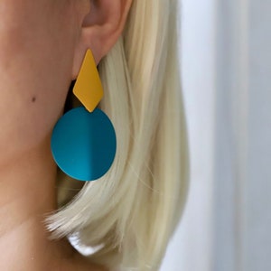 May include: A pair of geometric earrings with a teal blue circle and a yellow diamond shape.