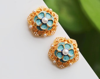 May include: A pair of gold-tone earrings with blue and white enamel flower designs. Each earring features a pearl in the center of the flower.
