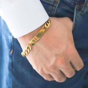 Puede incluir: Un brazalete de cadena dorada con una placa rectangular grabada con el nombre "Sheila".