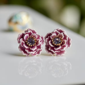 May include: A pair of purple flower-shaped earrings with a small purple rhinestone in the center of each flower.