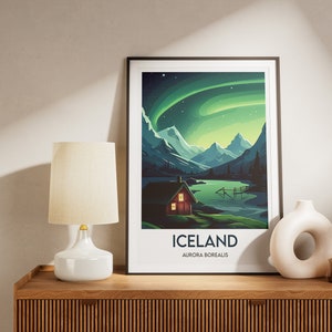 May include: A framed poster with a colorful illustration of a cabin in a mountain landscape with a lake and the aurora borealis in the sky. The poster has the text "ICELAND AURORA BOREALIS".