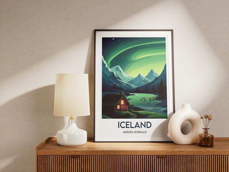 May include: A framed poster with a colorful illustration of a cabin in a mountain landscape with a lake and the aurora borealis in the sky. The poster has the text "ICELAND AURORA BOREALIS".