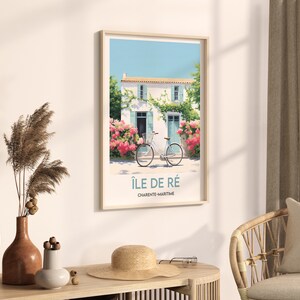 Op de afbeelding: Een ingelijste poster met een wit huis met blauwe luiken en een fiets ervoor. De poster heeft de tekst "&Icirc;le de R&eacute;" en "Charente-Maritime" erop.