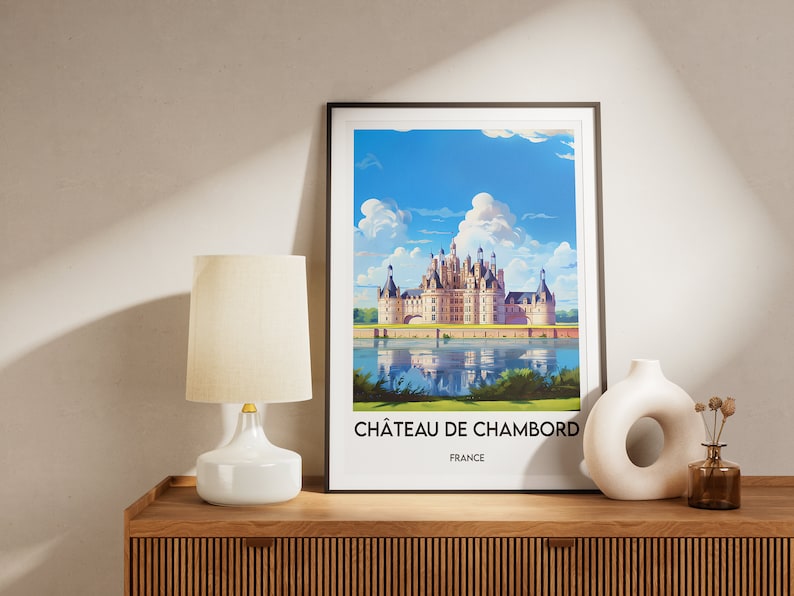 May include: A framed print of a painting depicting Ch&acirc;teau de Chambord, a large French castle with a moat and reflecting water. The text below the image reads "Ch&acirc;teau de Chambord, France".