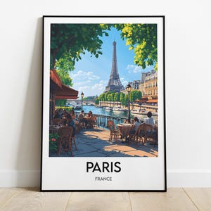 Puede incluir: Una ilustración enmarcada de una escena de café parisino con la Torre Eiffel en el fondo. El café está situado a orillas del Sena y presenta gente sentada en mesas bajo un dosel. La ilustración es de estilo minimalista con fondo blanco y marco negro. El texto "PARIS" y "FRANCE" está impreso debajo de la imagen.