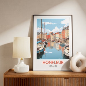 May include: A framed print of a colourful illustration of a harbour scene in Honfleur, Normandy, France. The print features a row of colourful buildings along the waterfront, with boats docked in the harbour. The text "Honfleur, Normandie" is printed below the image.