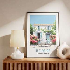 Op de afbeelding: Een ingelijste print van een wit huis met blauwe luiken en een fiets ervoor. Het huis is omgeven door roze bloemen en groene wijnstokken. De print is getiteld "&Icirc;le de R&eacute;, Charente-Maritime".