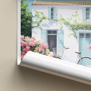 Op de afbeelding: Een wit huis met blauwe luiken en een witte fiets met een mand ervoor. Het huis is bedekt met groene wijnstokken en roze bloemen.