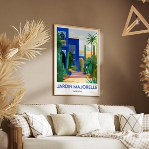 Pu&ograve; includere: Un poster incorniciato con un'illustrazione colorata di un edificio blu con un cortile e palme. Il testo "JARDIN MAJORELLE MAROCCO" &egrave; in fondo al poster.