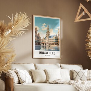 May include: A framed poster with a vintage travel illustration of the Grand Place in Brussels, Belgium. The poster has a white background with a blue sky and white clouds. The text "BRUXELLES BELGIQUE" is printed in black at the bottom of the poster.