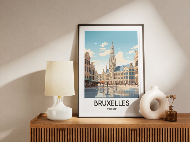May include: A framed print of a colorful illustration of the Grand Place in Brussels, Belgium. The print features a view of the city square with the Town Hall in the center. The text "BRUXELLES BELGIQUE" is printed below the image.