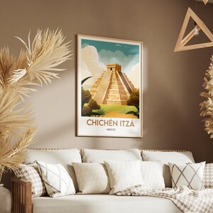 May include: A vintage-style poster with a colorful illustration of the Chichen Itza pyramid in Mexico. The poster has a brown frame and is hanging on a beige wall.