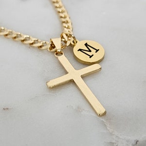 May include: Gold chain necklace with a gold cross pendant and a small gold circle pendant with the letter "M" engraved on it.