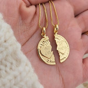 May include: Two gold necklaces, each featuring a pendant shaped like a broken heart. One pendant reads "BE FRI" and the other reads "ST ENDS". The pendants have a heart design and are attached to fine gold chains.