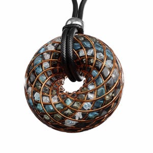 May include: A pendant necklace featuring a spherical, open-centered design. The pendant is crafted with a copper-colored wire frame, filled with blue, gray, and clear stones. A black cord with a silver-toned clasp suspends the pendant.