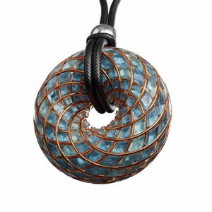 May include: A pendant necklace featuring a circular, open-center design. The pendant is composed of blue-green glass tiles set within a copper-colored metal frame. The necklace has a black cord with a silver-colored clasp.