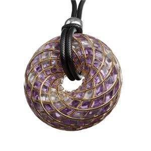 May include: A gold pendant necklace with a circular design featuring a swirling pattern of amethyst and clear crystals. The pendant is suspended from a black leather cord.
