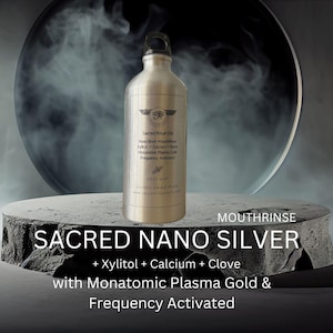 May include: A silver-colored bottle of "Sacred Nano Silver" mouthrinse. The bottle has a black cap and is labeled with text including "Xylitol + Calcium + Clove" and "Frequency Activated". The product is displayed on a gray, textured platform.