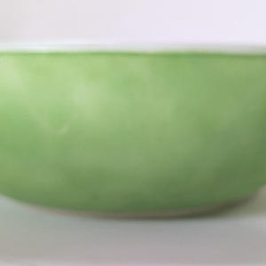 May include: A light green ceramic bowl with a white rim. The bowl has a rounded shape and a smooth surface. The bowl is designed for food preparation or serving.