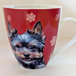 May include: Red ceramic mug featuring a Yorkshire Terrier dog portrait and white snowflake designs. The mug has a white handle and a glossy finish, perfect for hot beverages.