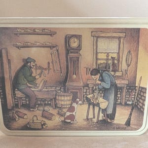 May include: Rectangular tin with a painted illustration of a shoemaker's workshop. Two figures are working on shoes, with a dog, clock, and tools visible. The scene is set in a rustic workshop with a window and a broom.