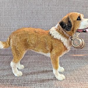 May include: A detailed figurine of a Saint Bernard dog, standing with its mouth slightly open. The dog has brown and white fur, with a small wooden barrel around its neck. The figurine is a decorative item.