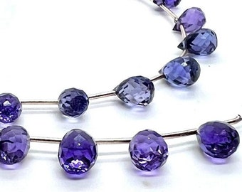 May include: A strand of purple amethyst gemstone beads, each bead is faceted and shaped like a teardrop. The beads are strung on a silver wire.