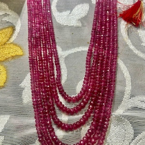 May include: A multi-strand necklace made of deep pink faceted beads. The necklace is made of several strands of beads, and the beads are all the same size and shape.