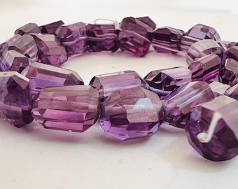 May include: A strand of faceted amethyst beads, each bead is a deep purple color and has a faceted, geometric shape. The beads are strung together to form a necklace or bracelet.