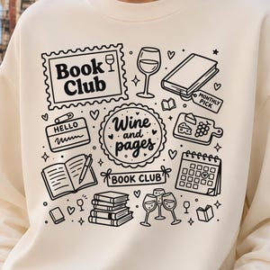 May include: Cream-colored sweatshirt with a black graphic design featuring the words "Book Club" and "Wine and Pages." The design includes illustrations of books, wine glasses, and a calendar. The person is wearing blue jeans.
