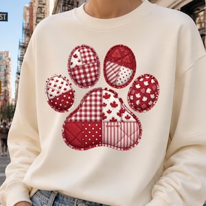 Può includere: Felpa color crema con un grande design a zampa di patchwork nei toni del rosso. La zampa è composta da vari motivi, tra cui pois, quadri e foglie d'acero. La felpa è abbinata a jeans di denim blu chiaro.