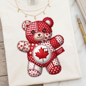 Può includere: T-shirt color crema con un design di orsacchiotto patchwork rosso e bianco, con un emblema a forma di foglia d'acero e la scritta "CANADA DAY". Una collana d'oro con ciondoli a forma di stella e luna è drappeggiata sulla maglietta.