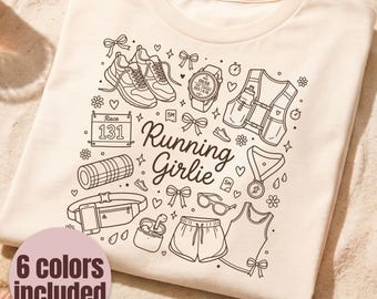 May include: Cream-colored t-shirt with a black line drawing of running-related items, including shoes, a watch, shorts, and a medal. The words "Running Girlie" are in the center. A pink circle at the bottom left says "6 colors included."