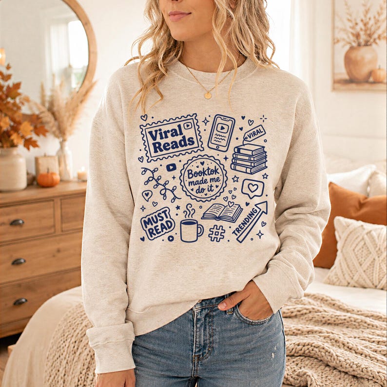 May include: A light beige sweatshirt with a blue graphic design featuring the words "Viral Reads," "Booktok made me do it," and other book-related icons. The design includes hearts, a coffee cup, and a trending arrow.