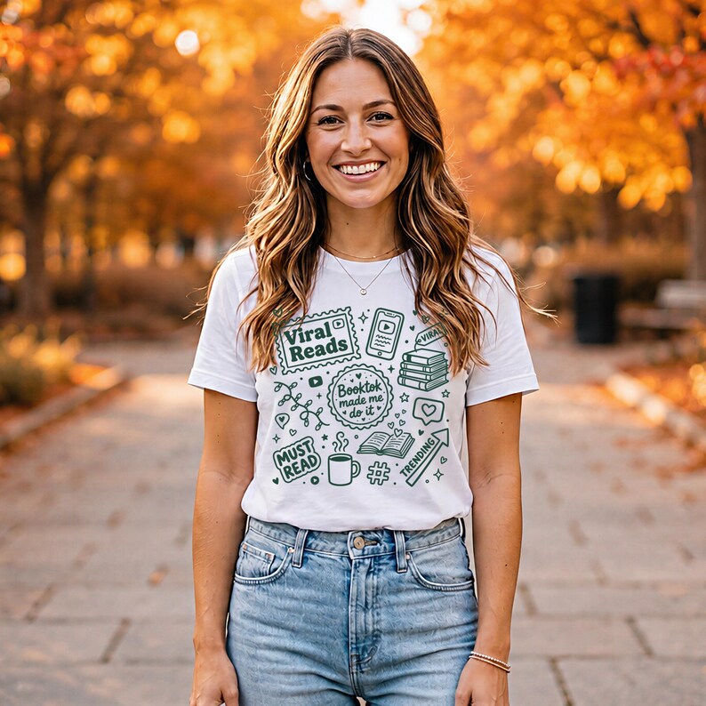 May include: White t-shirt with green graphics and text. The shirt features the words "Viral Reads," "Booktok made me do it," and other book-related icons. The person is wearing blue jeans.