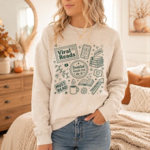 May include: A light gray sweatshirt with a green graphic design featuring the words "Viral Reads," "Booktok made me do it," and "Must Read." The design includes book stacks, a coffee mug, and a trending arrow.