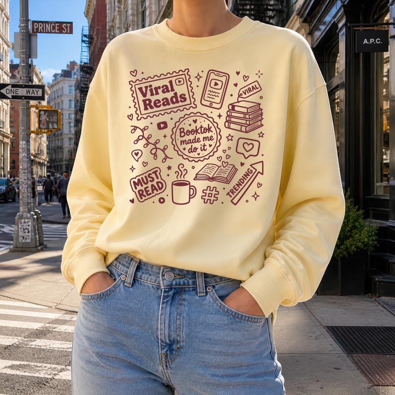 May include: A light yellow sweatshirt with a maroon graphic design featuring the words "Viral Reads," "Booktok made me do it," and "Must Read." The design includes book-related icons and the word "Trending."