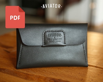 Puede incluir: Un estuche de cuero negro de estilo sobre con una solapa cosida y un logotipo que dice "AVIATOR - Handcrafted & Built to Last - Est. 2015."