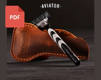 Puede incluir: Una maquinilla de afeitar negra y plateada con un mango blanco y negro en una funda de cuero marrón con el texto "SPADAR - MEN'S PRODUCTS -" grabado en relieve en la funda. La maquinilla de afeitar está etiquetada como "AVIATOR".