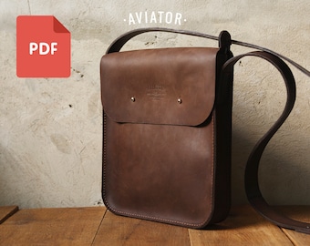 Puede incluir: Un bolso de hombro de cuero marrón con cierre de solapa y una correa. El bolso tiene un remache de metal en la parte delantera y el texto "AVIATOR" está impreso sobre el bolso.